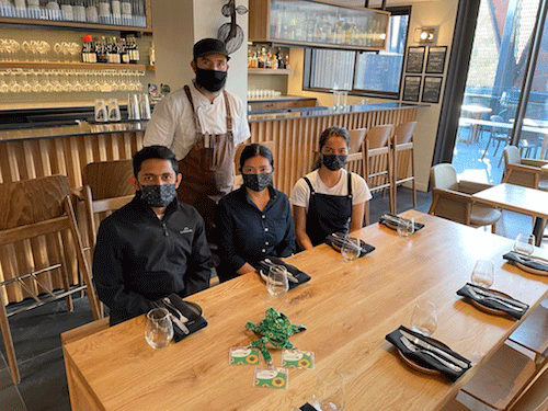 Four hotel staff wearing face coverings sat a table with one more staff member standing behind them 
