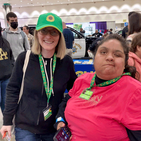 Holly Tyrer wears the Hidden Disabilities Sunflower lanyard and baseball cap. She is smiling at the camera. Next to Holly is Gelsey Garcia, also wearing the Sunflower lanyard, who Holly met at the Abilities Expo.
