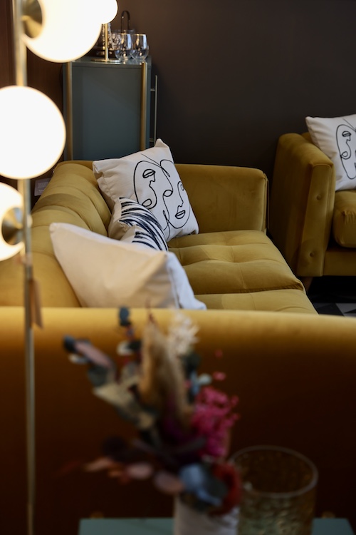 An image of a yellow sofa. There are white scatter cushions on the sofa. 