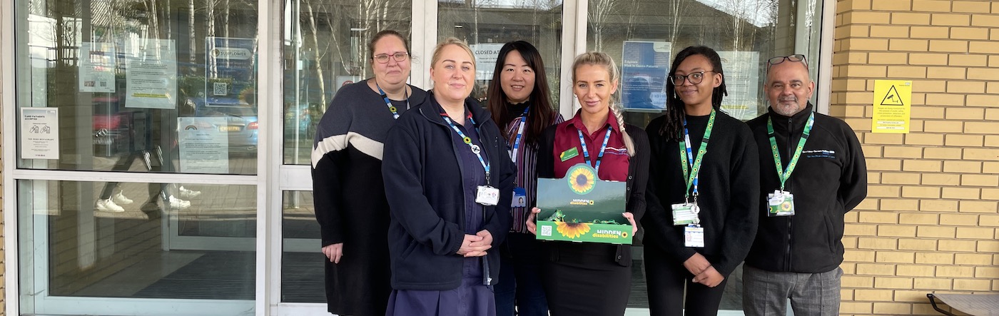 A group of female colleagues stand in front of an NHS walk in centre holding a box of Sunflower lanyards 